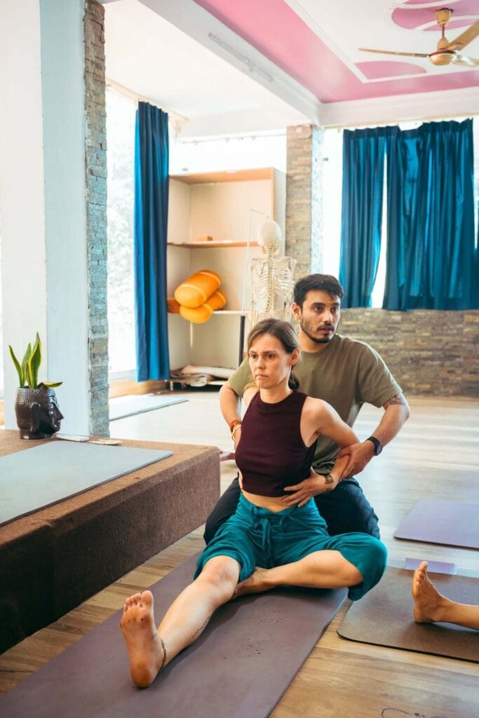 Yoga teacher adjusting student posture
